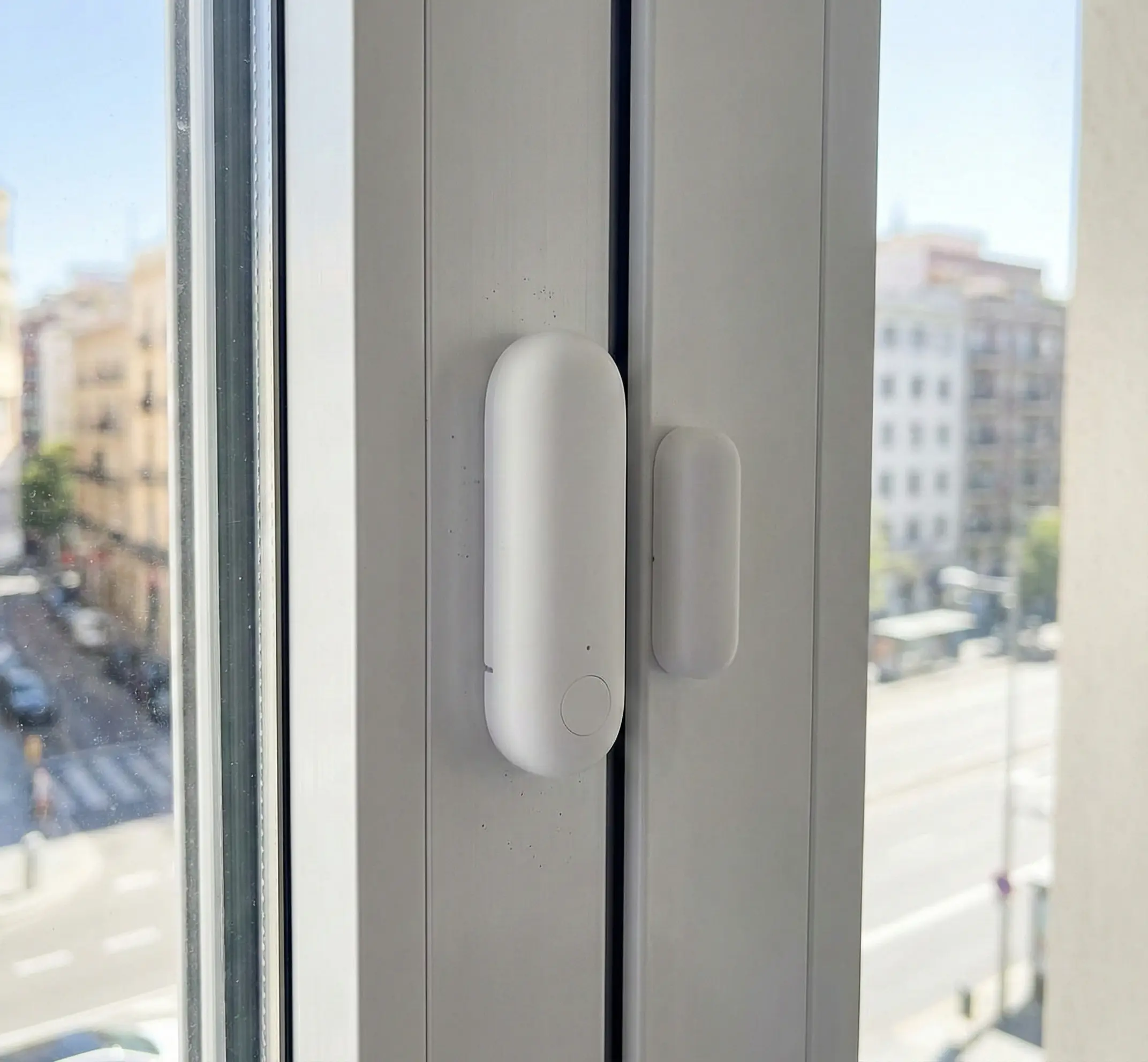 Primer plano de un sensor de ventana Aqara inteligente de color blanco instalado en un marco de aluminio de un apartamento turístico