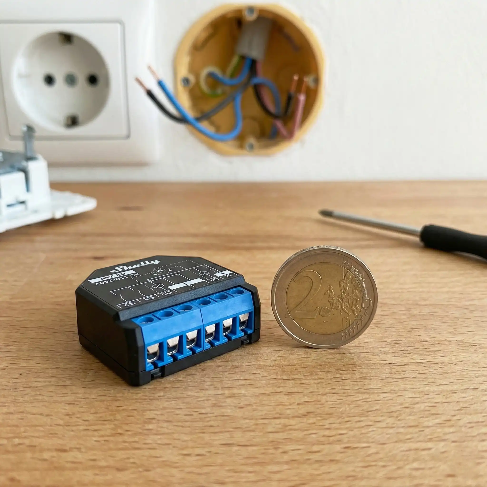 Módulo inteligente Shelly Plus 2PM comparado con una moneda de 2 euros para mostrar su tamaño minúsculo, ideal para empotrar en cajetines de pared estrechos