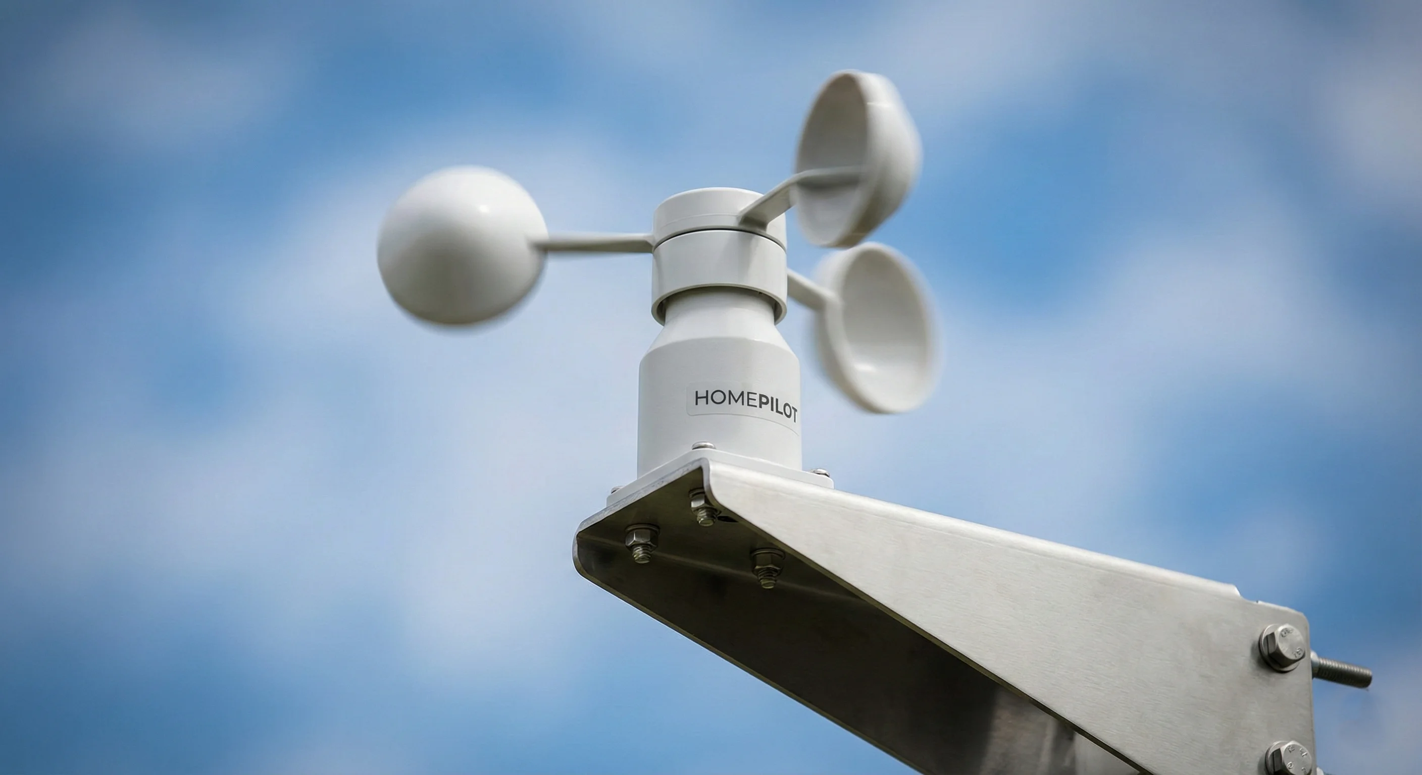 Sensor de luminosidad y viento profesional instalado en una fachada moderna, protegiendo un toldo de gran tamaño bajo un sol intenso de mediodía. Fotografía arquitectónica limpia y luminosa.