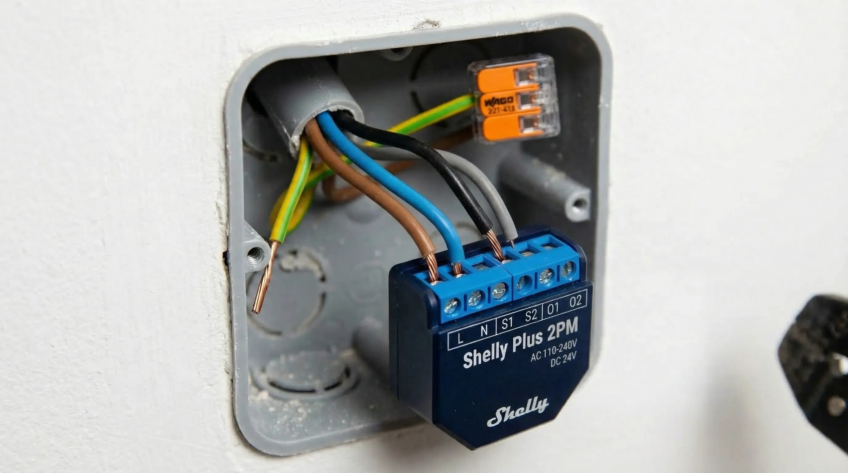 Instalación técnica de un relé Shelly Plus 2PM en una caja de mecanismos eléctrica estándar española, mostrando las conexiones de cables de cobre y el diseño compacto del dispositivo azul