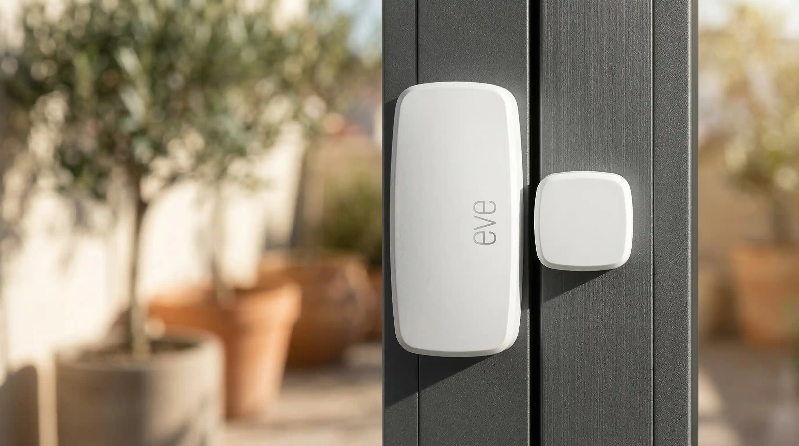 Sensor de ventana en carpintería de aluminio | PROMPT: Fotografía macro profesional de un sensor de contacto Matter blanco con acabado mate sedoso, instalado sobre carpintería de aluminio anodizado gris antracita. Enfoque nítido en la unión de los sensores, fondo muy desenfocado mostrando una terraza mediterránea bañada por el sol. Iluminación natural de alto contraste, estética limpia y tecnológica, calidad de catálogo de arquitectura, 8k.